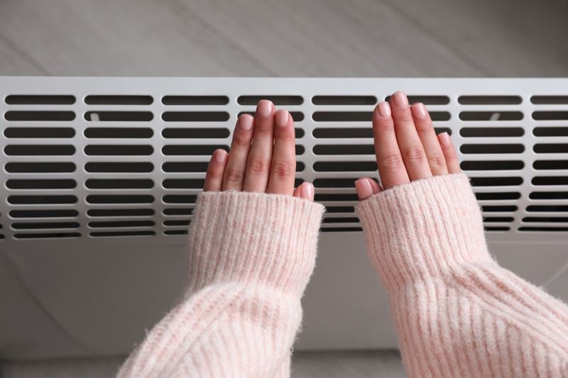 A close-up of a woman warming her hands near an electric heater.